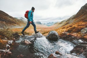 A man hiking and crossing a river.