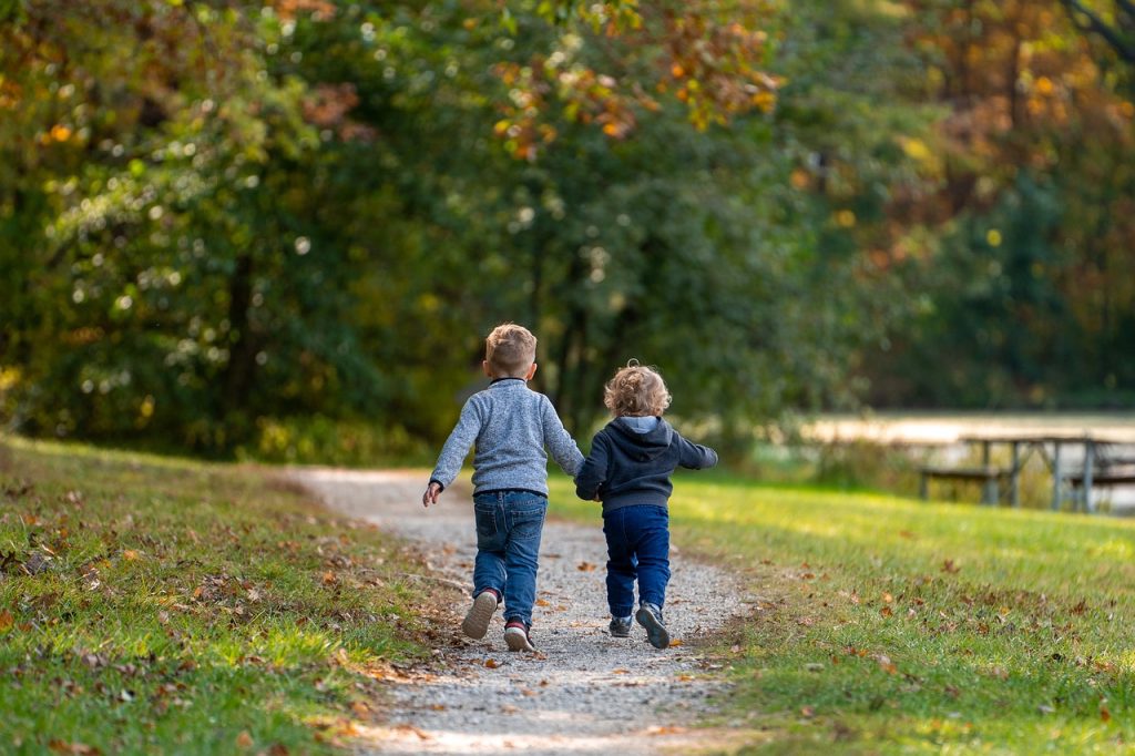 Two children holding hands walking down a park path.