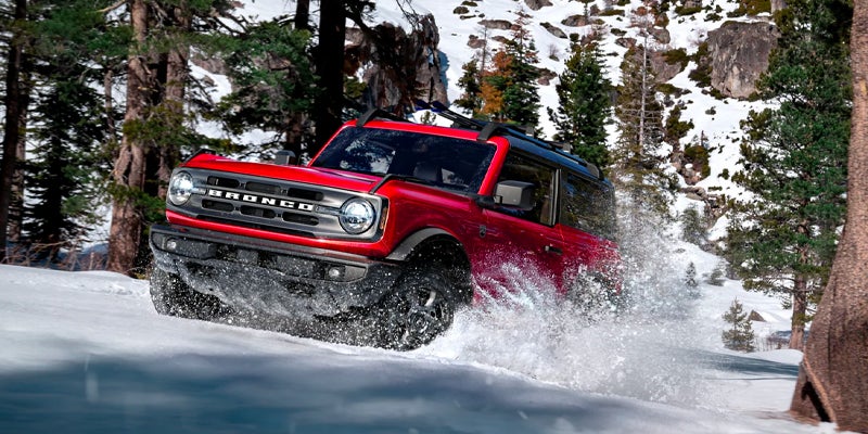 A red 2023 Ford Bronco driving through snow.