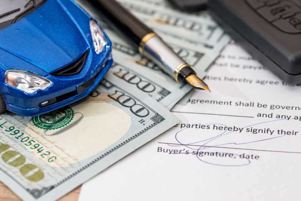 A car loan agreement with a toy car, money, a pen, and the buyer's signature on the document.