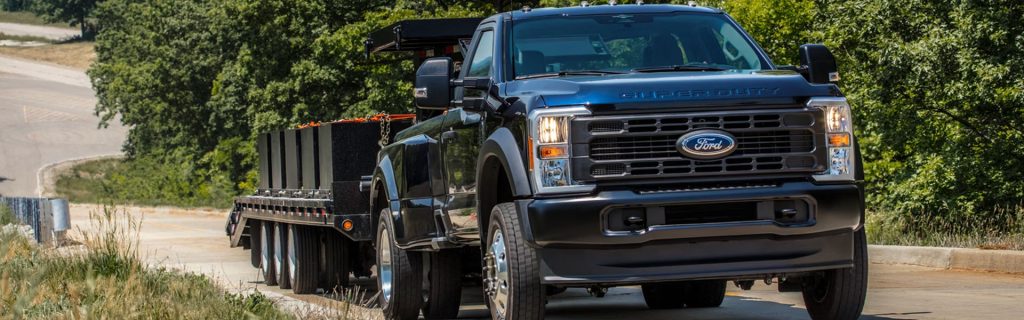 Black Ford Super Duty truck towing a heavy trailer on a road