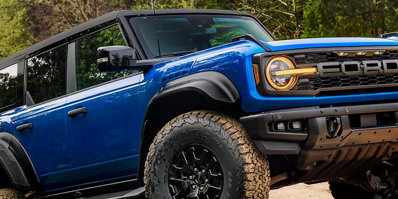 Blue Ford Bronco parked on a wooded trail.